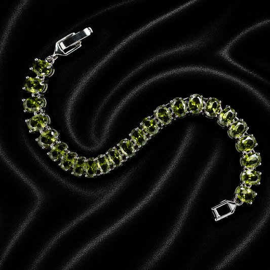 A silver tennis bracelet featuring round green peridot gemstones, displayed on a black satin fabric background.