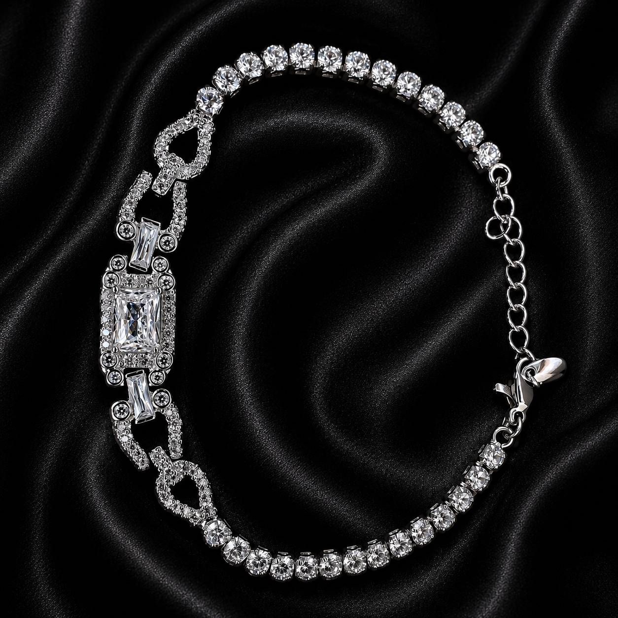 A silver-tone tennis bracelet with clear gemstones, featuring a central rectangular emerald-cut stone and decorative links, displayed on a black satin fabric background.