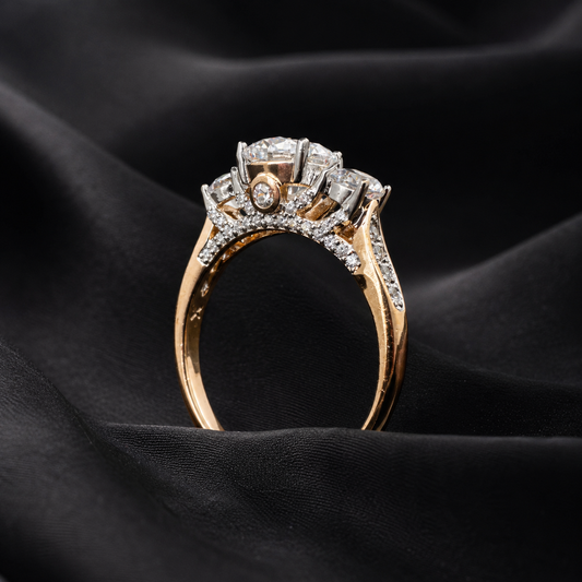 A yellow gold ring with a three-stone diamond engagement setting, resting on draped black satin fabric.