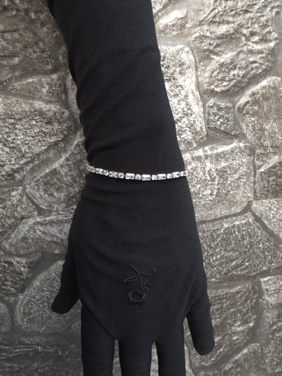 Hand wearing a black glove with a silver bracelet on a textured pavement background