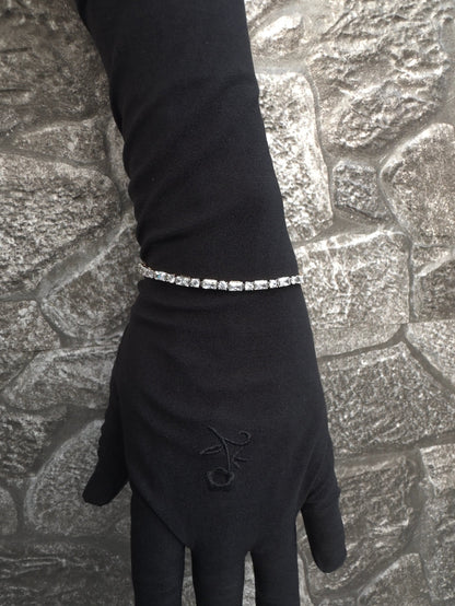 Hand wearing a black glove with a silver bracelet on a textured pavement background