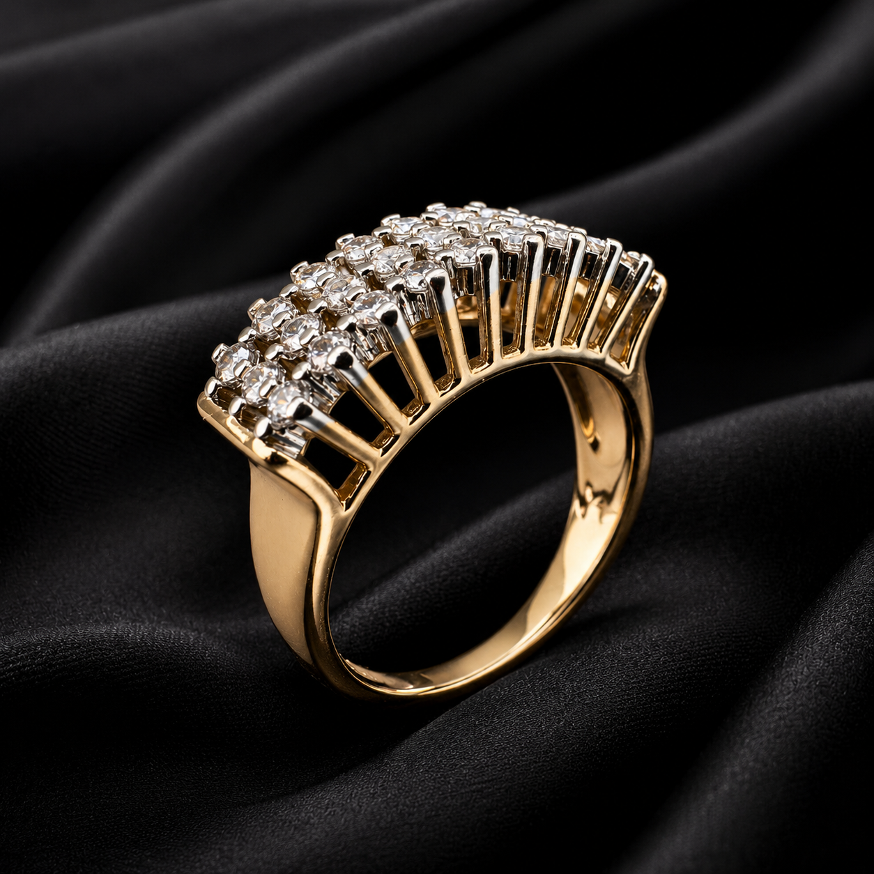 A gold ring with a wide, fan-like top set with clear gemstones, displayed on a draped black fabric background.