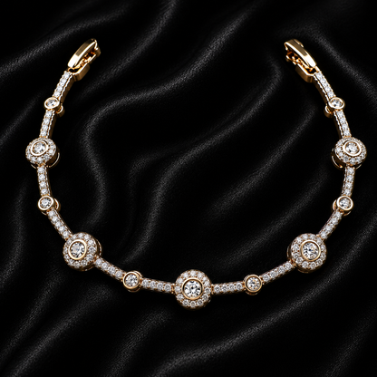 A gold-plated tennis bracelet adorned with clear round-cut gemstones, displayed on a black satin fabric background.