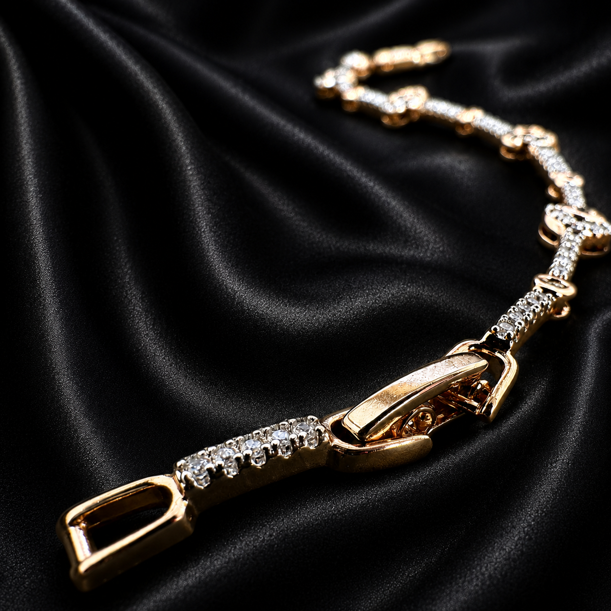 A gold-tone chain bracelet embellished with clear rhinestones, displayed on a draped black satin fabric background.