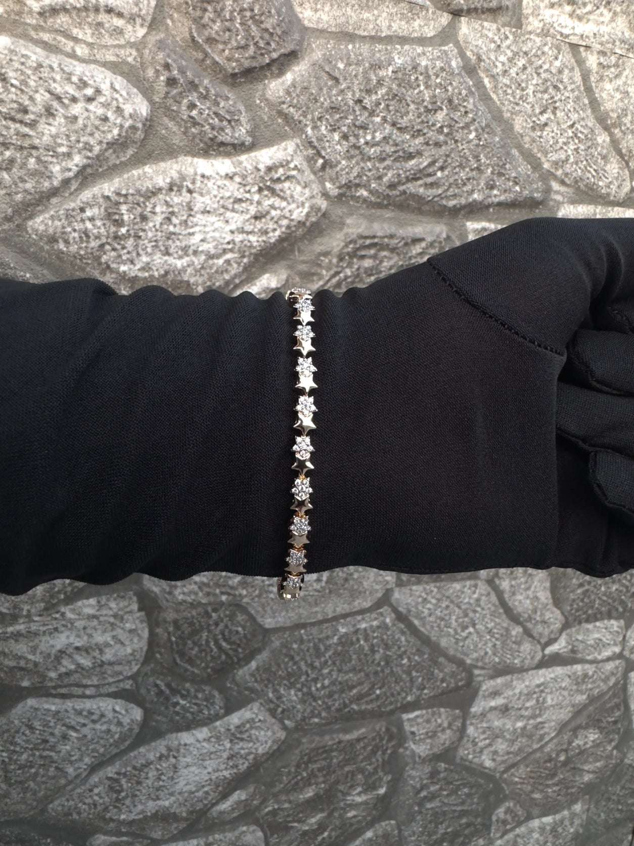 Bracelet with small stones on a person's wrist against a textured stone wall background