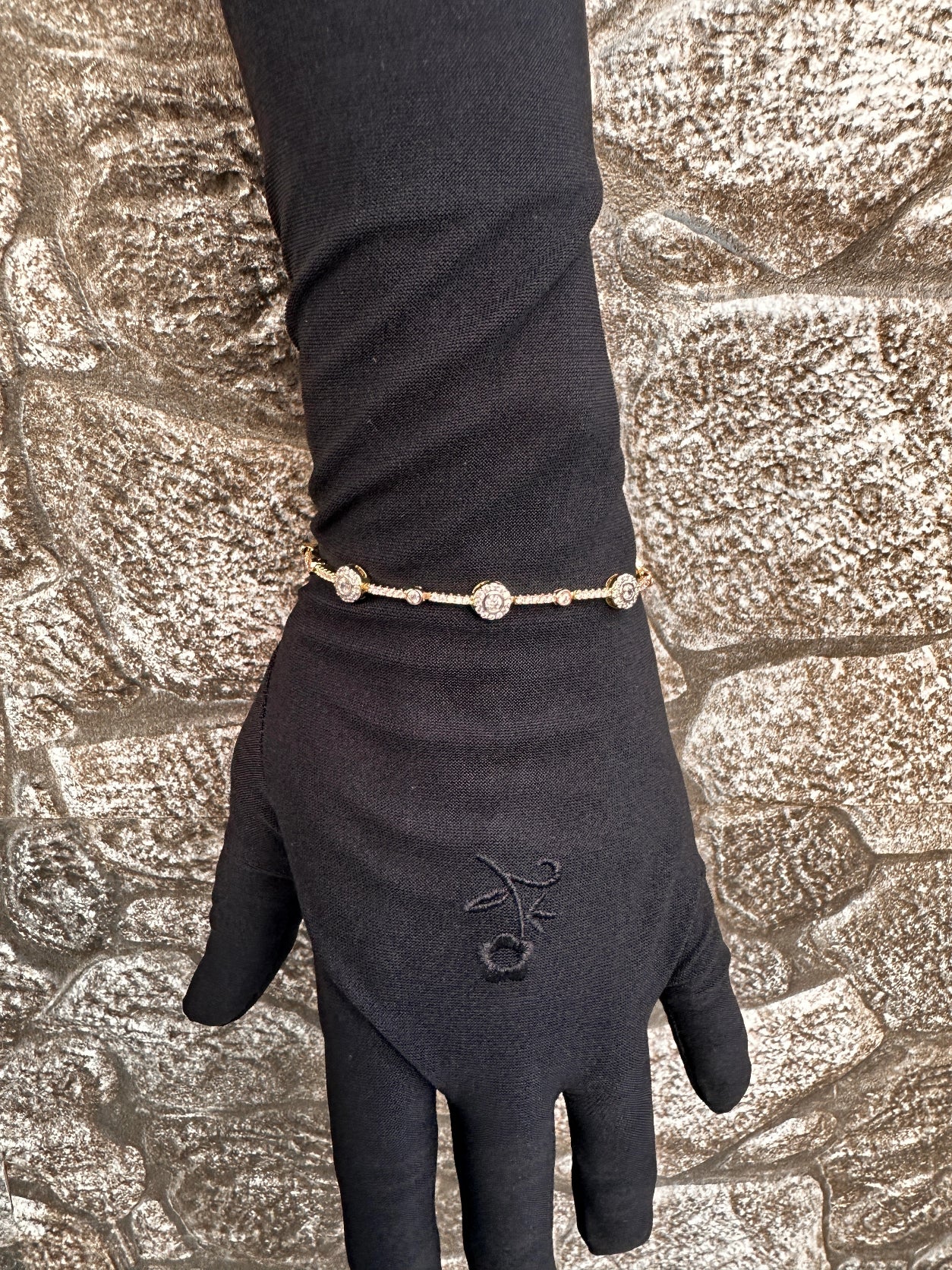 Black glove with a gold bracelet on a textured stone background