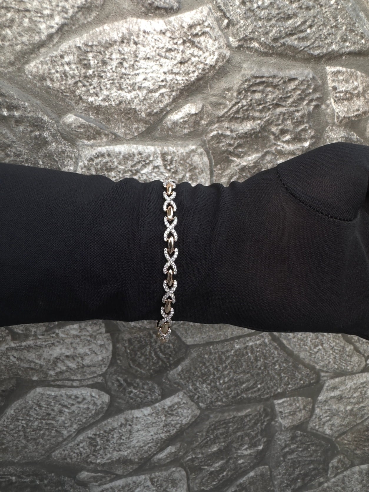 Silver chain bracelet on a black wrist against a stone wall background