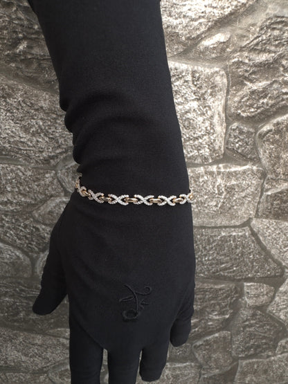 Hand wearing a black glove with a gold bracelet against a textured stone wall background