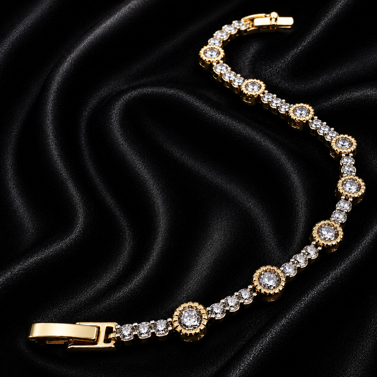 A gold-plated tennis bracelet with clear round-cut gemstones, arranged on a draped black satin fabric background.