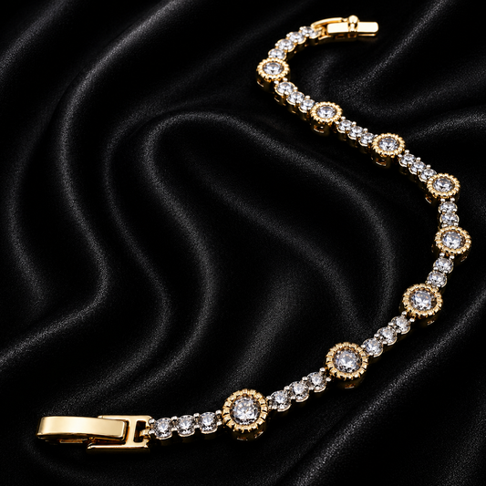 A gold-plated tennis bracelet with clear round-cut gemstones, arranged on a draped black satin fabric background.