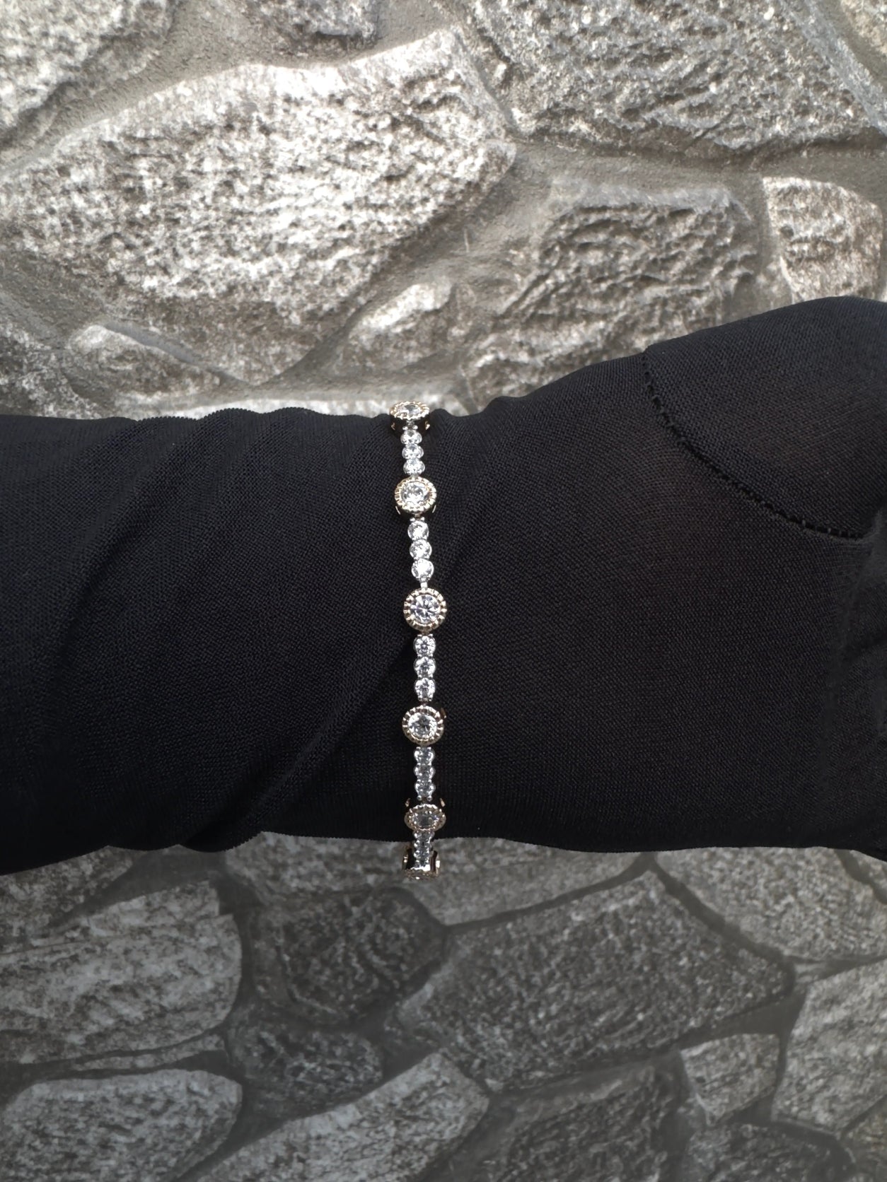 Silver bracelet on a black glove against a textured gray background