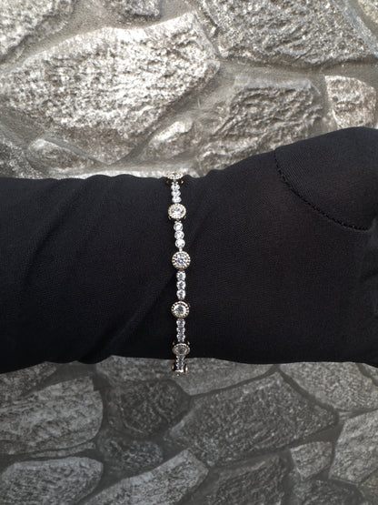 Silver bracelet on a black glove against a textured gray background