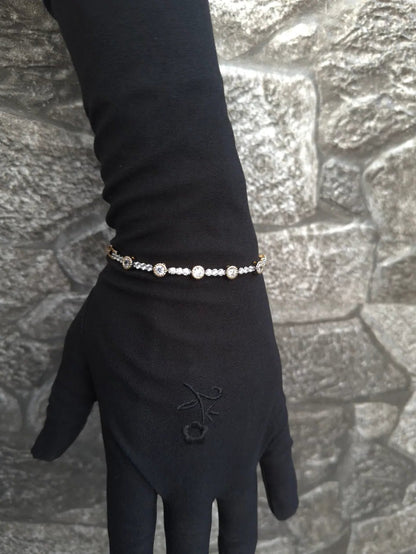 Hand wearing a black glove with a bracelet against a stone wall background