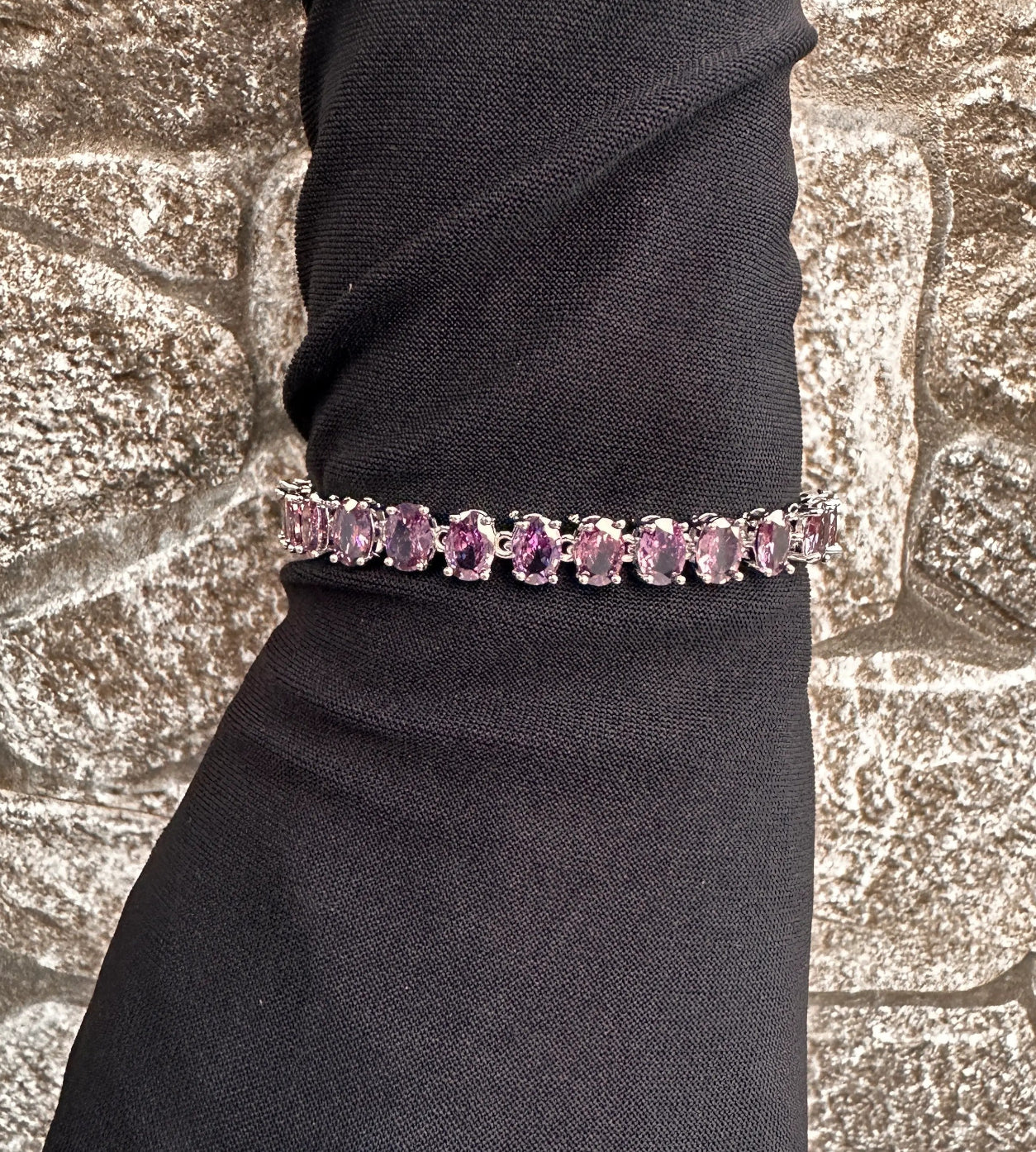 Purple gemstone bracelet on a black wrist against a textured stone background