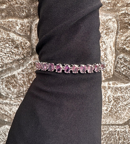Purple gemstone bracelet on a black wrist against a textured stone background