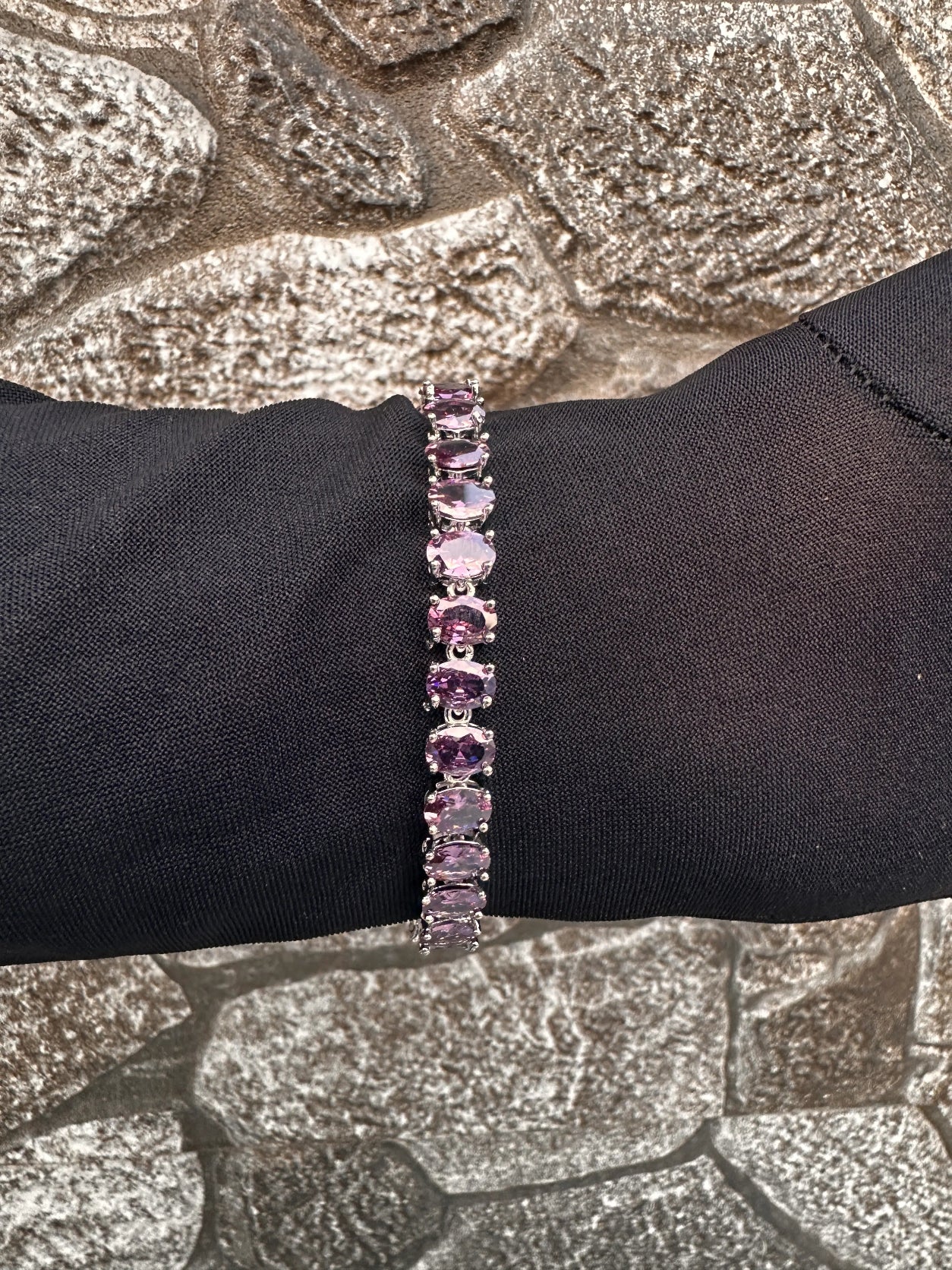 Purple gemstone bracelet on a black wrist against a textured stone background