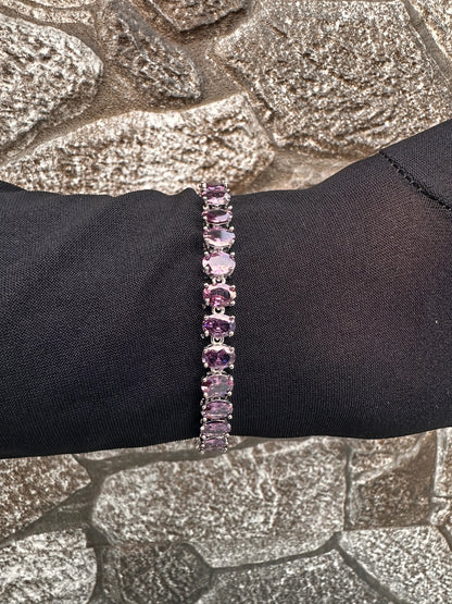 Purple gemstone bracelet on a black wrist against a textured stone background