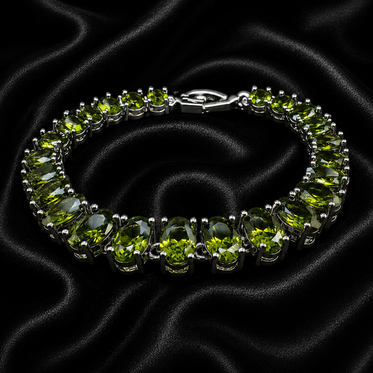 A silver tennis bracelet featuring oval-cut green peridot gemstones, displayed on a draped black satin fabric background.