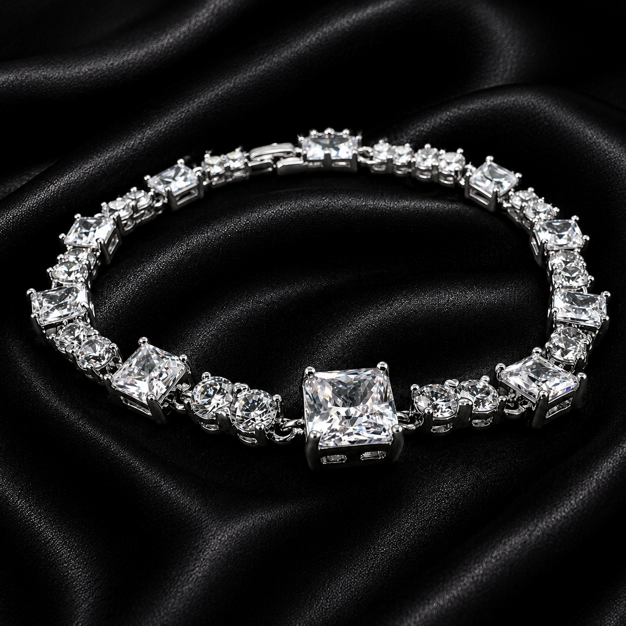 A silver-toned tennis bracelet featuring a large princess-cut clear center stone and multiple clear rectangular and round accent stones, displayed on a draped black satin fabric background.