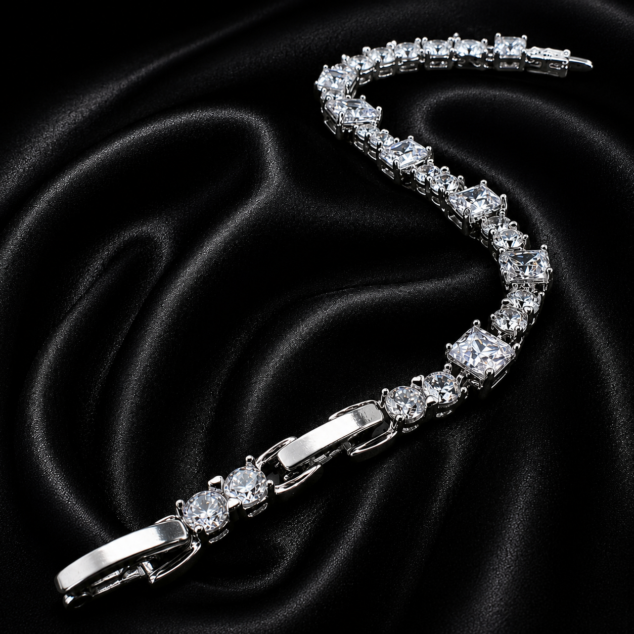 A silver tennis bracelet with clear round-cut stones, arranged in a curved S-shape on a black satin fabric background.