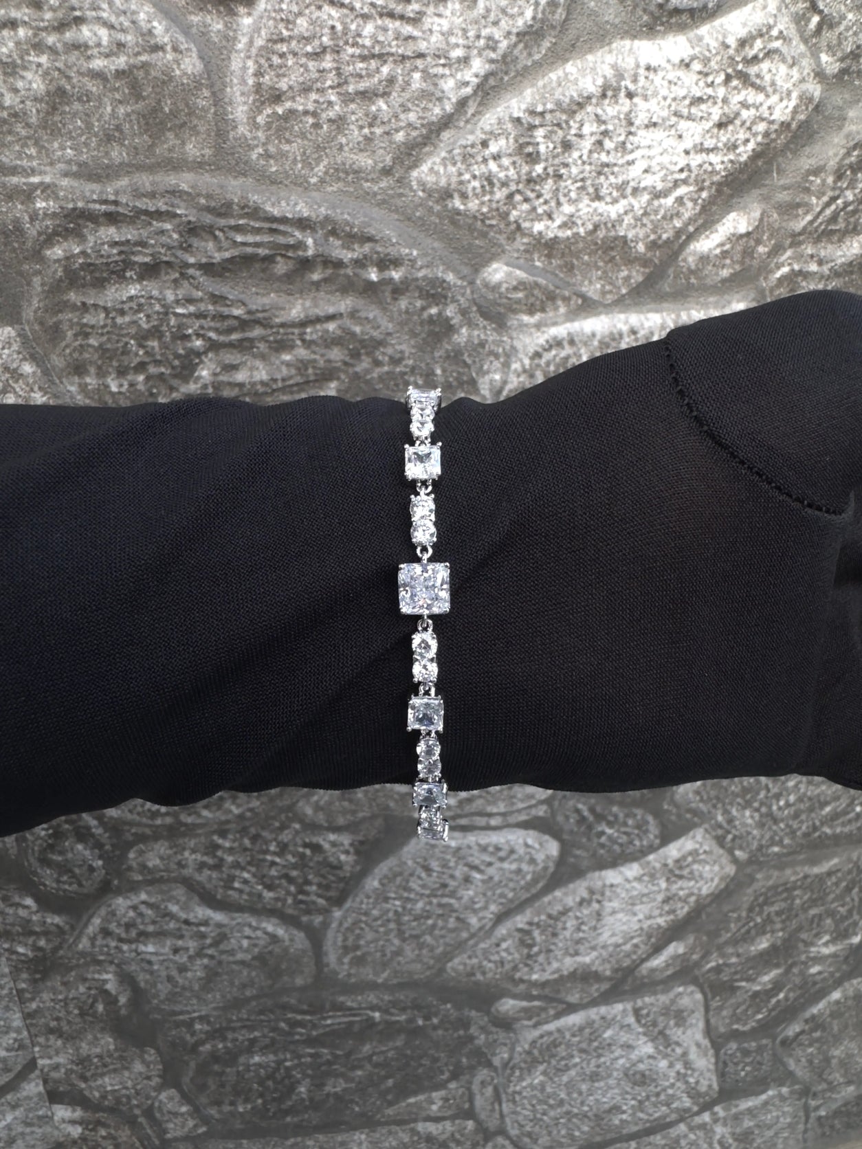 Diamond bracelet on a black dress against a textured silver background