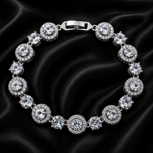 A silver-toned tennis bracelet with round clear gemstones in halo settings, displayed on a black satin fabric background.