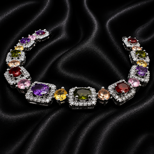 A multi-stone silver-toned necklace featuring large, colorful gemstones in red, purple, green, yellow, pink, and orange, set in silver-toned metal and displayed on a black satin background.