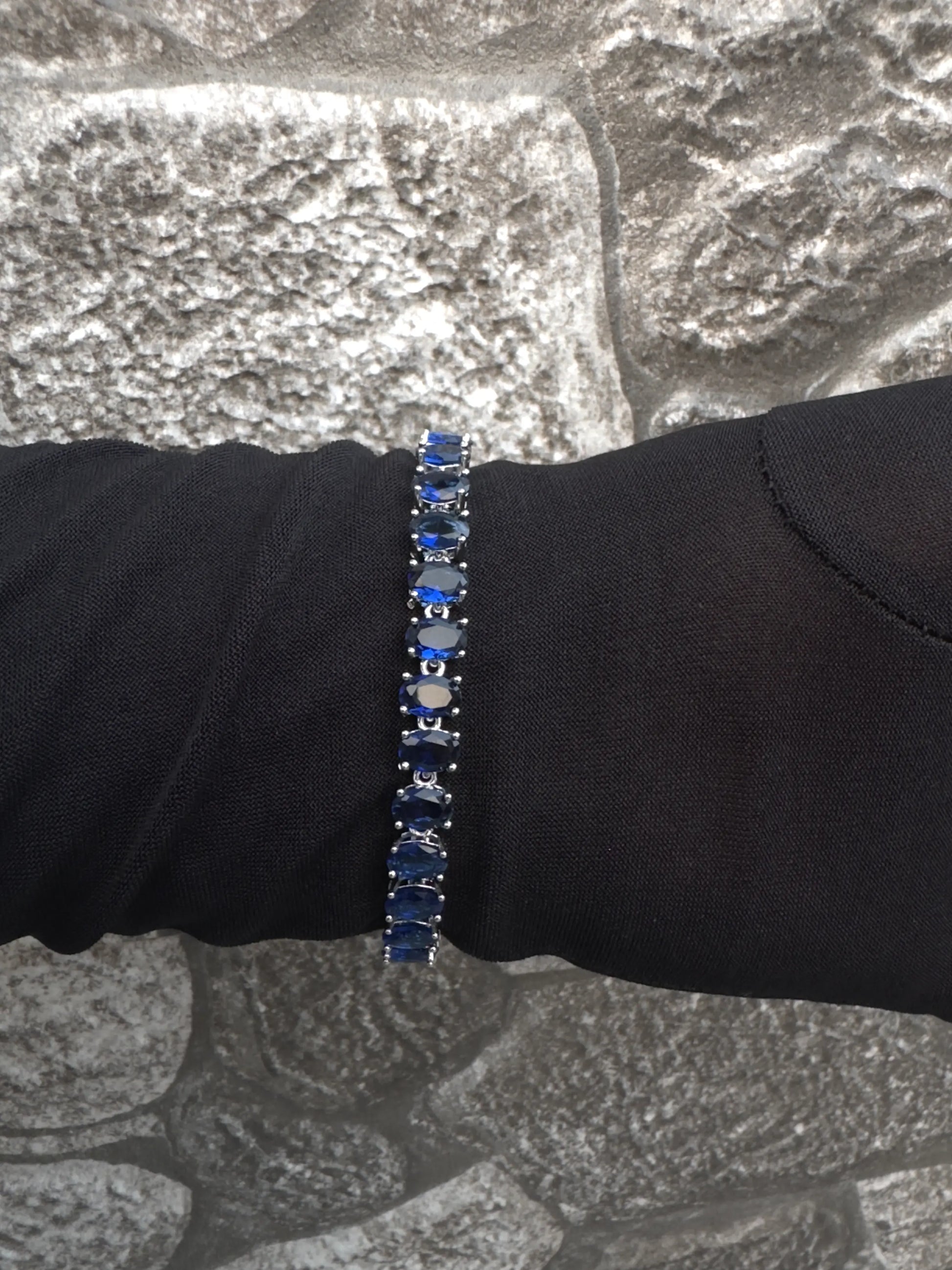 Bracelet with blue stones on a black sleeve against a stone wall background