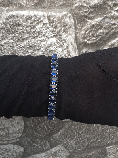 Bracelet with blue stones on a black sleeve against a stone wall background