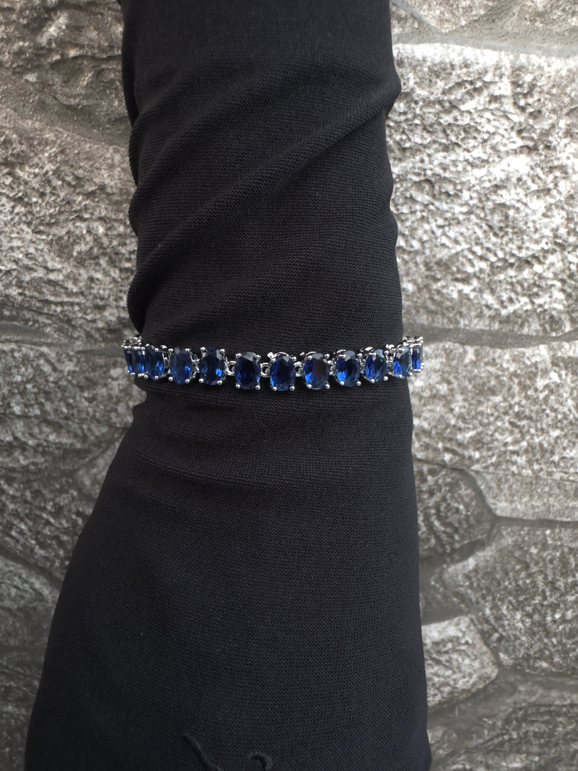 Bracelet with blue stones on a black sleeve against a textured gray background