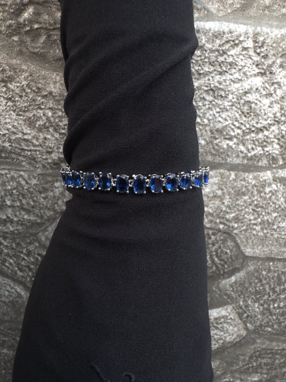 Bracelet with blue stones on a black sleeve against a textured gray background