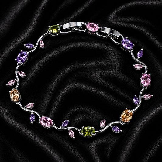 A silver-toned vine-style bracelet with multiple colored gemstones, displayed on a black satin fabric background. The bracelet features oval and marquise-cut stones in pink, purple, green, and peach-orange.