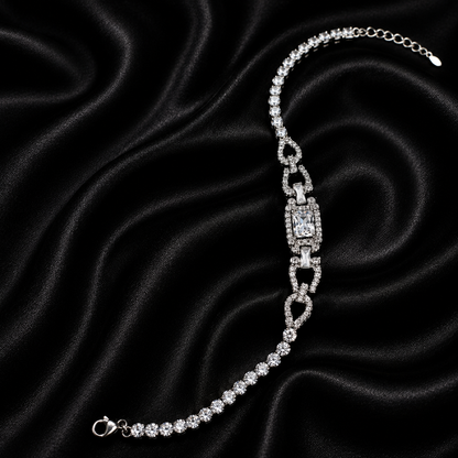 A silver-toned chain bracelet with a central rectangular pavé-style link and smaller repeating links, displayed on a black satin fabric background.