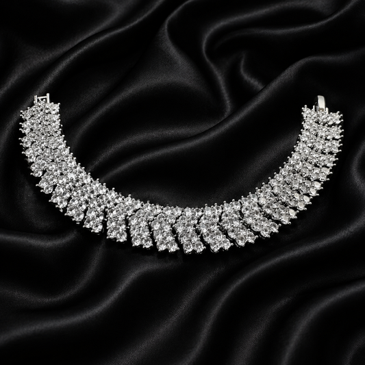 A silver-toned diamond tennis necklace displayed on a draped black satin fabric background.