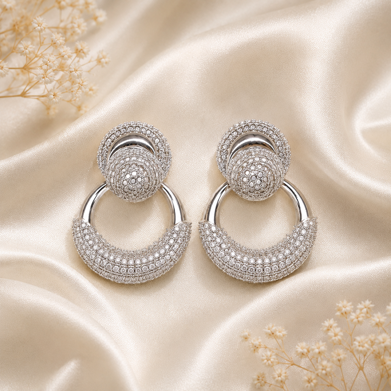 Silver earrings with intricate designs on a satin surface