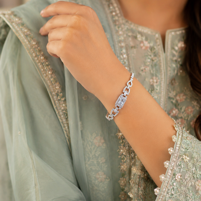 A close-up of a woman's wrist wearing a silver chain bracelet with clear stones, paired with a light sage green embroidered traditional outfit.